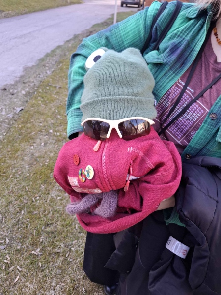 Aleksandra holder maskot med rosa kropp, et par solbriller, og en grønn lue med froskeøyne