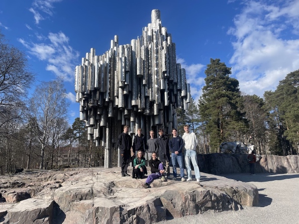Gruppebilde ved monument bestående av sølvfargede metallrør